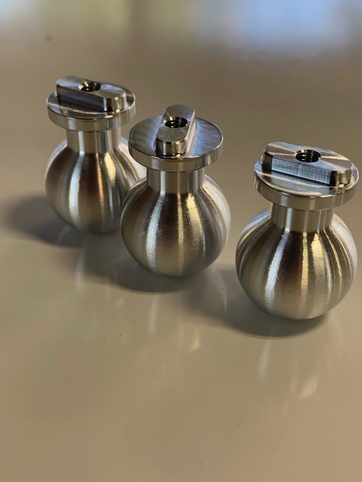 Three precision-turned stainless steel bell-shaped components machined by TXSwiss to plus or minus 0.0001 inch tolerance on a Swiss CNC lathe
