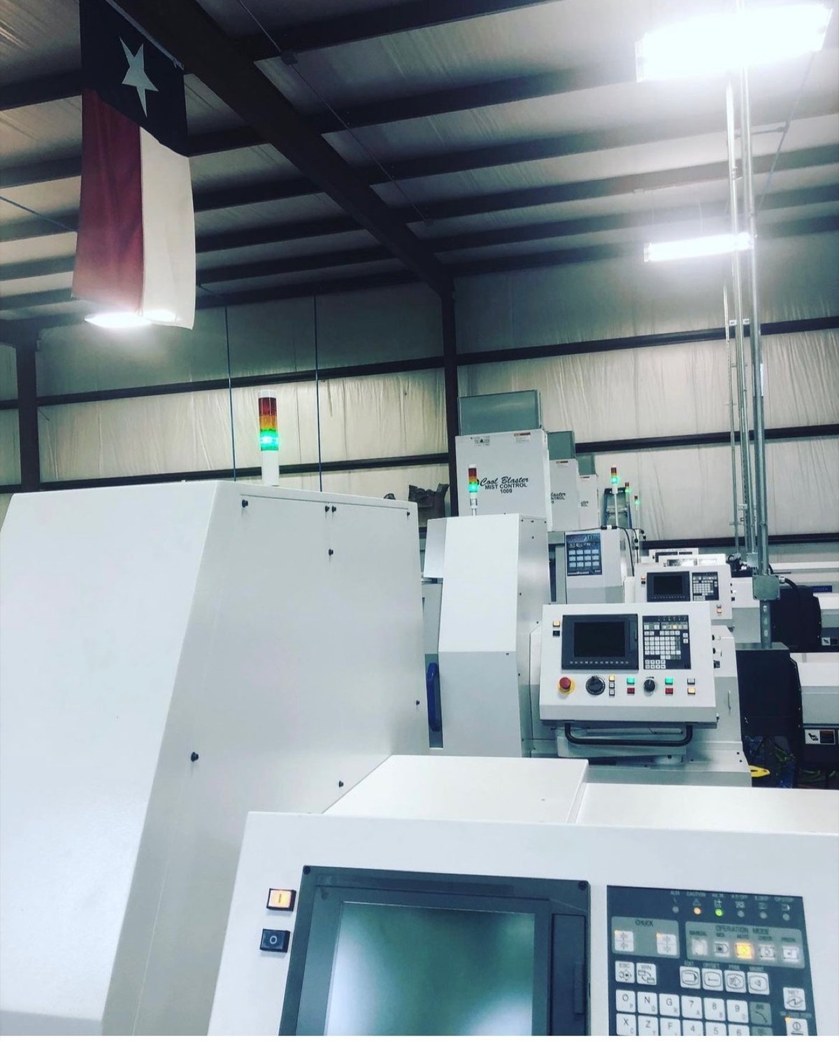 Row of Swiss CNC machines at TXSwiss with Texas flag overhead, Conroe, Texas precision manufacturing facility